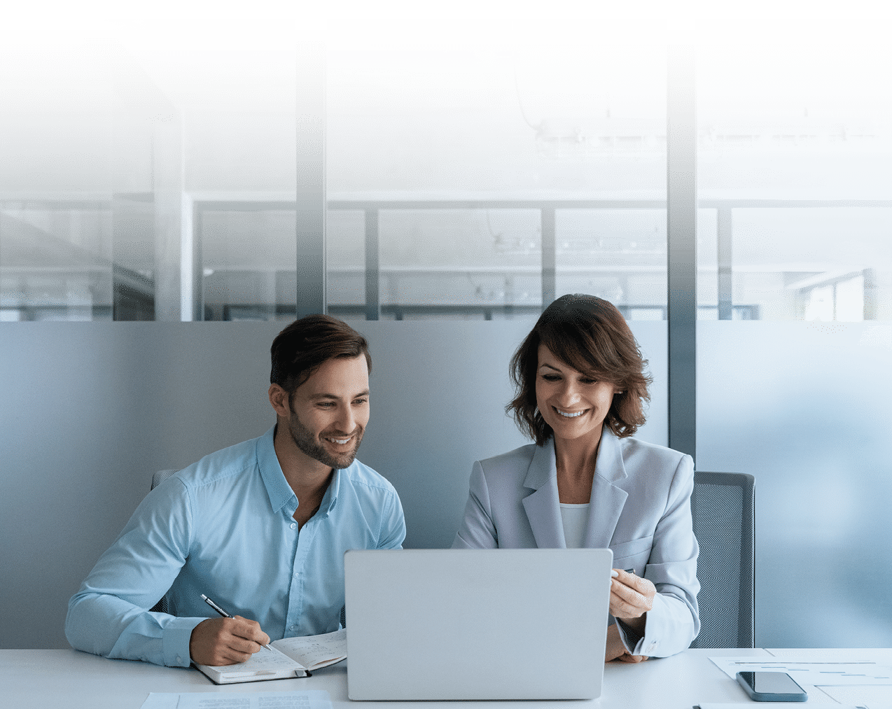 Latin mature professional ceo woman and European young student man at work in office. Team of two businesswoman and businessman working together using digital laptop pc, talking about business project